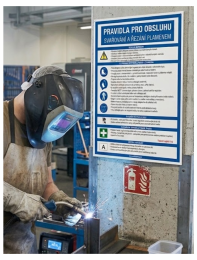 Welder in protective gear sparks flying while welding metal on a workbench in a workshop with safety posters on the wall